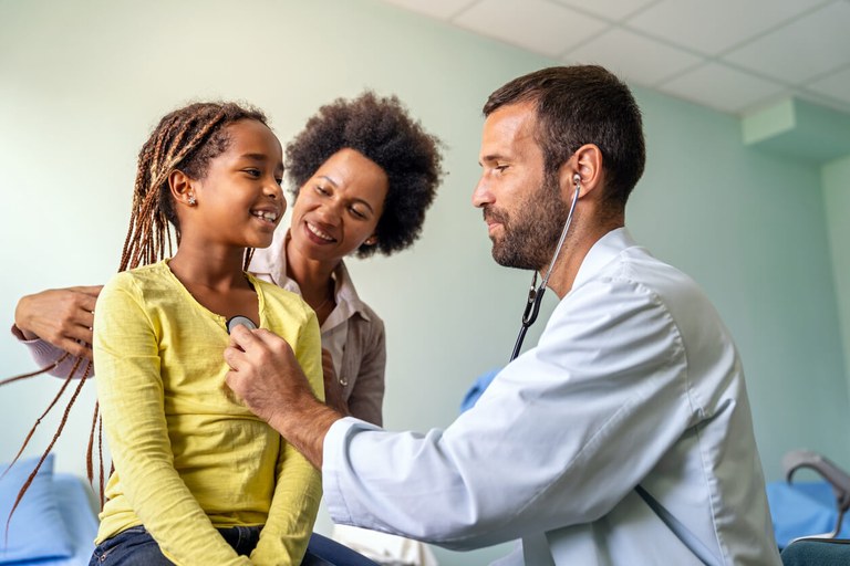 A-cheerful-girl-with-her-mother-and-a-male-family-medicine-doctor-wearing-a-stethoscope-during-her-routine-health-screenings.jpg